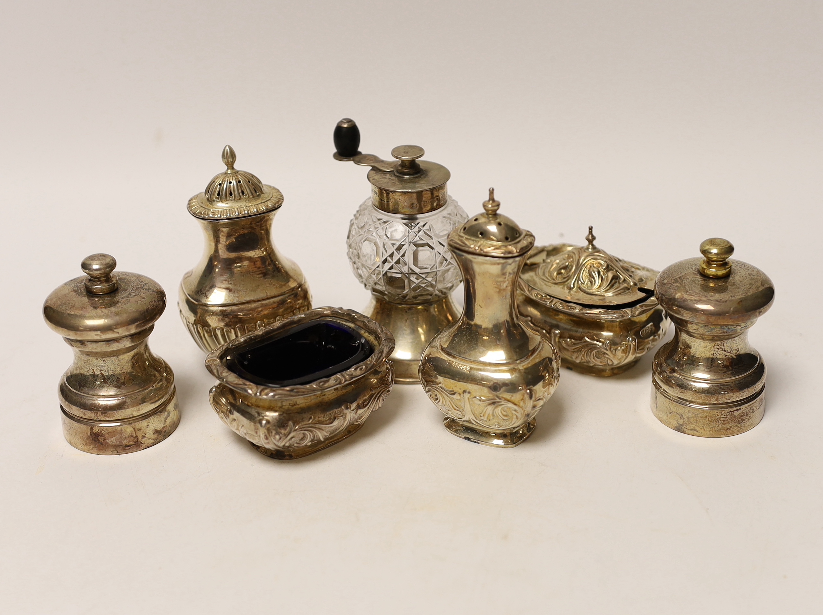 Seven assorted silver condiments, including a pepper grinder and salt and pepper mills.